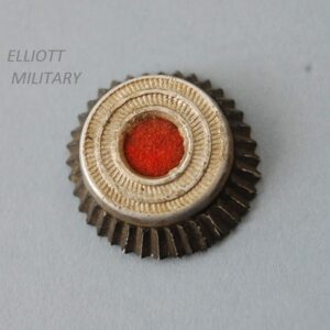 small circular cap badge with red centre surrounded by silver and blac