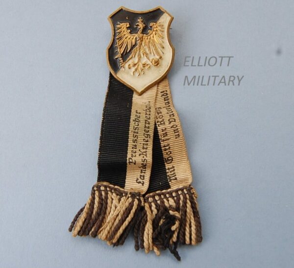 Pin badge with eagle on a black and white shield with ribbons attached